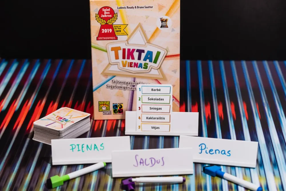 Tamsus fonas, ant stalo žaidimo dė-utė, rašikliai ir žaidimo kortelės.